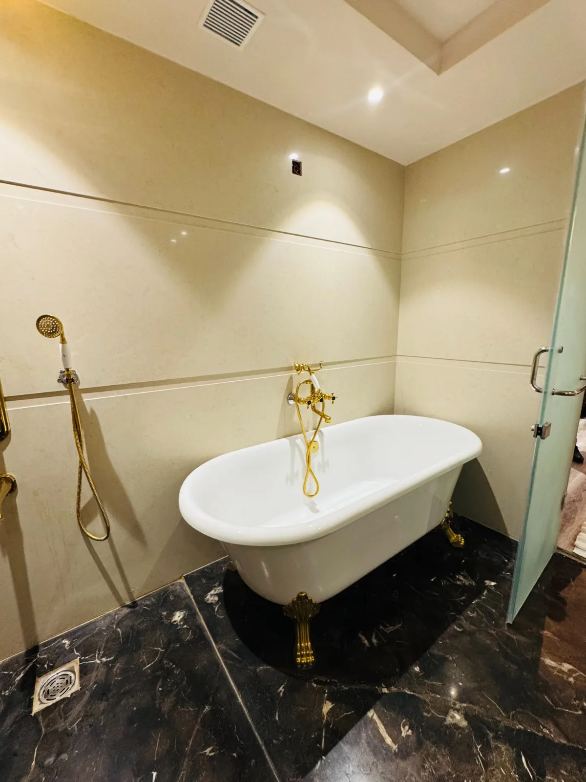 Freestanding clawfoot bathtub with gold claw feet and a gold telephone-style filler, on black veined marble in a suite bathroom at Vetiver Grand, Jabalpur.