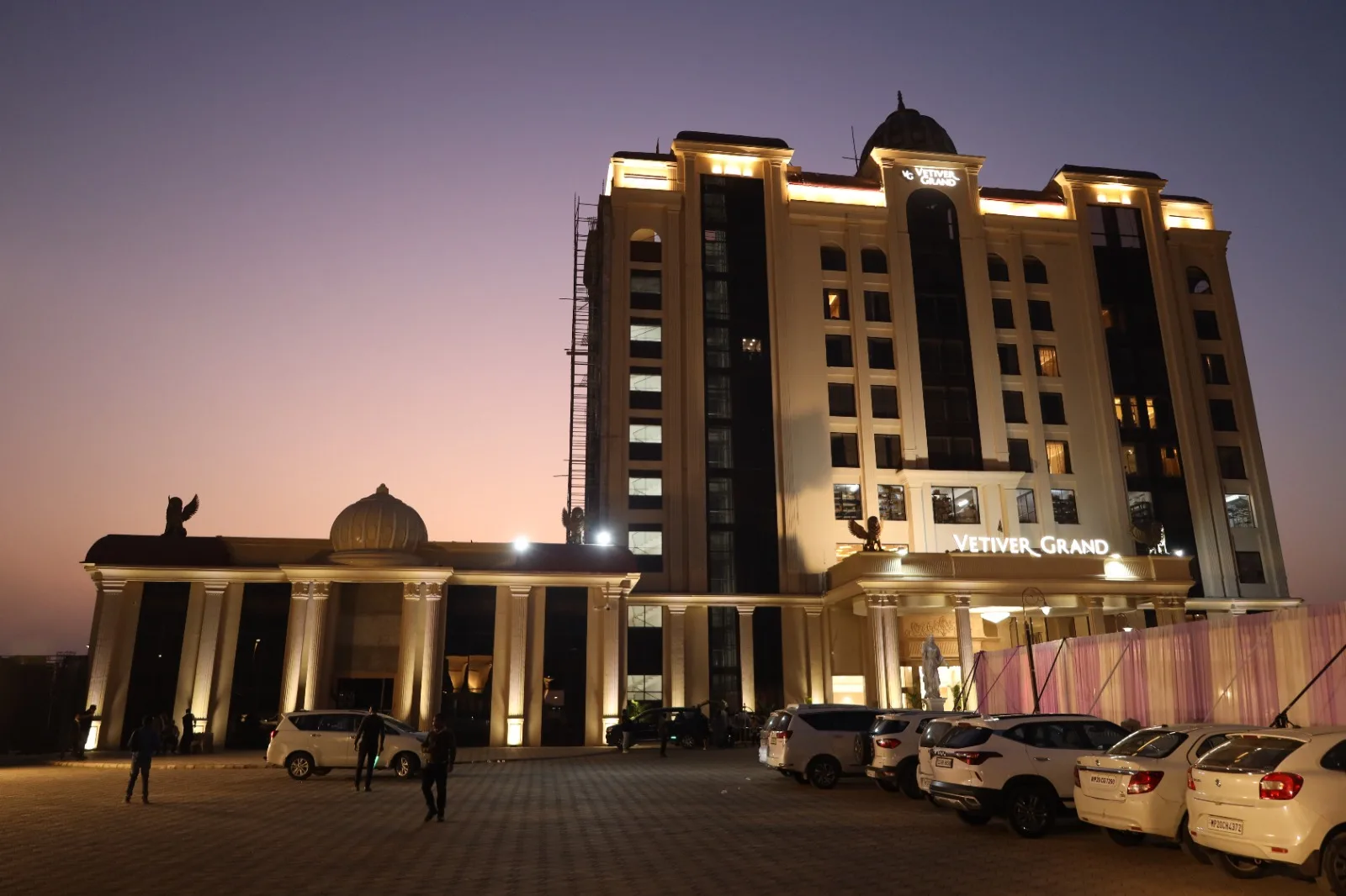 Vetiver Grand at dusk in Jabalpur: nine lit floors above the porte-cochère as cars arrive for an evening event.
