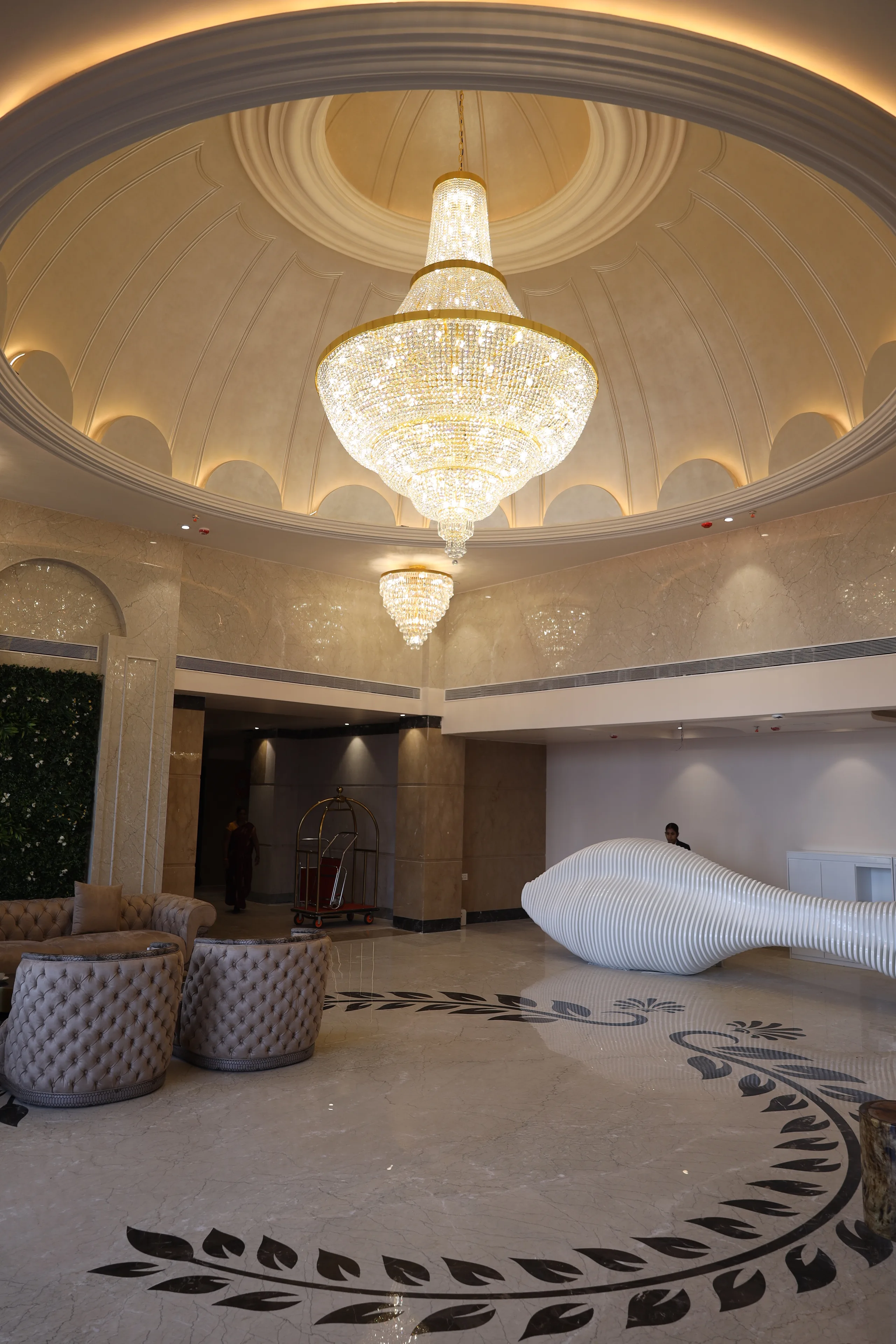 Lobby of Vetiver Grand, Jabalpur: crystal chandelier hanging from the gold-ribbed dome above the sculptural white reception desk and inlaid marble floor.