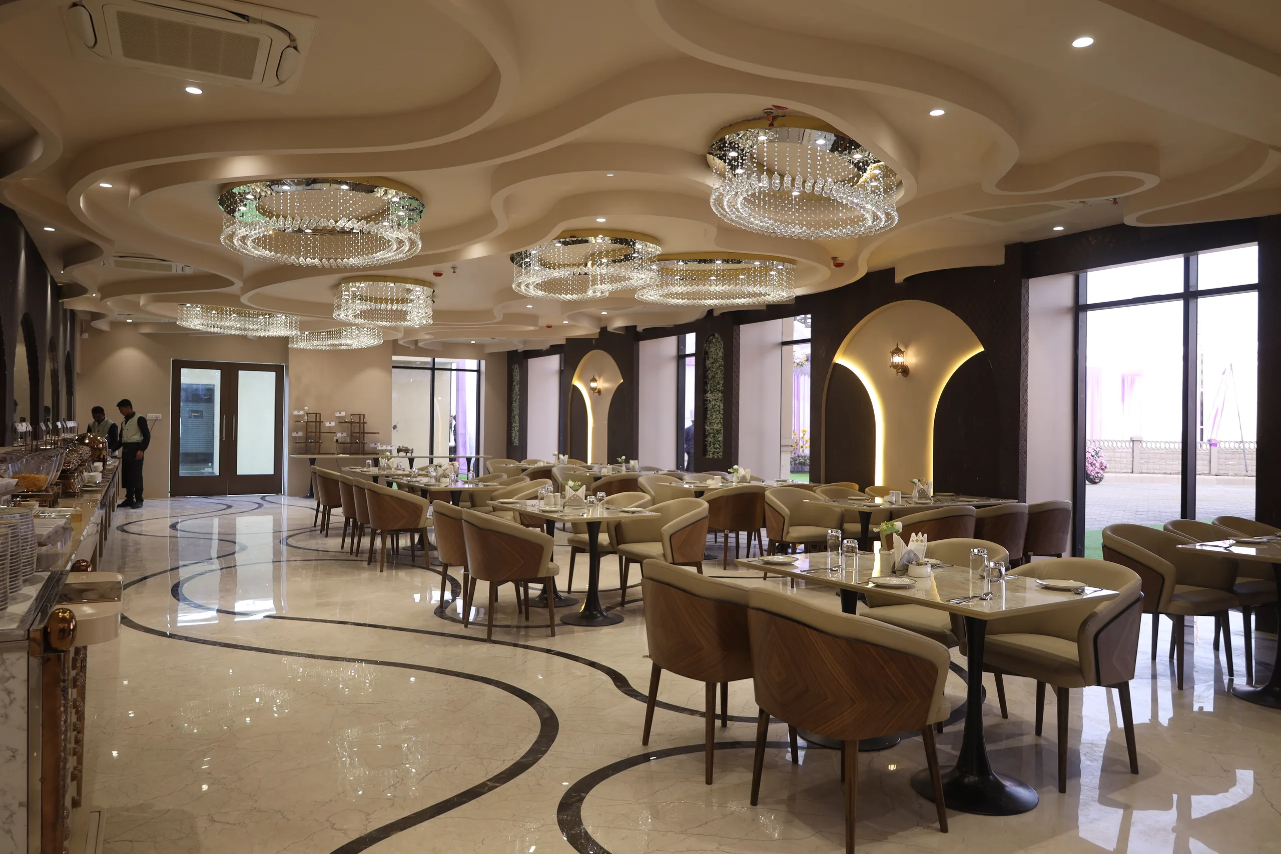 Kasturi, the pure vegetarian fine-dining restaurant on the ground floor of Vetiver Grand, Jabalpur: crystal chandeliers over marble inlay floors and arched, lantern-lit alcoves.