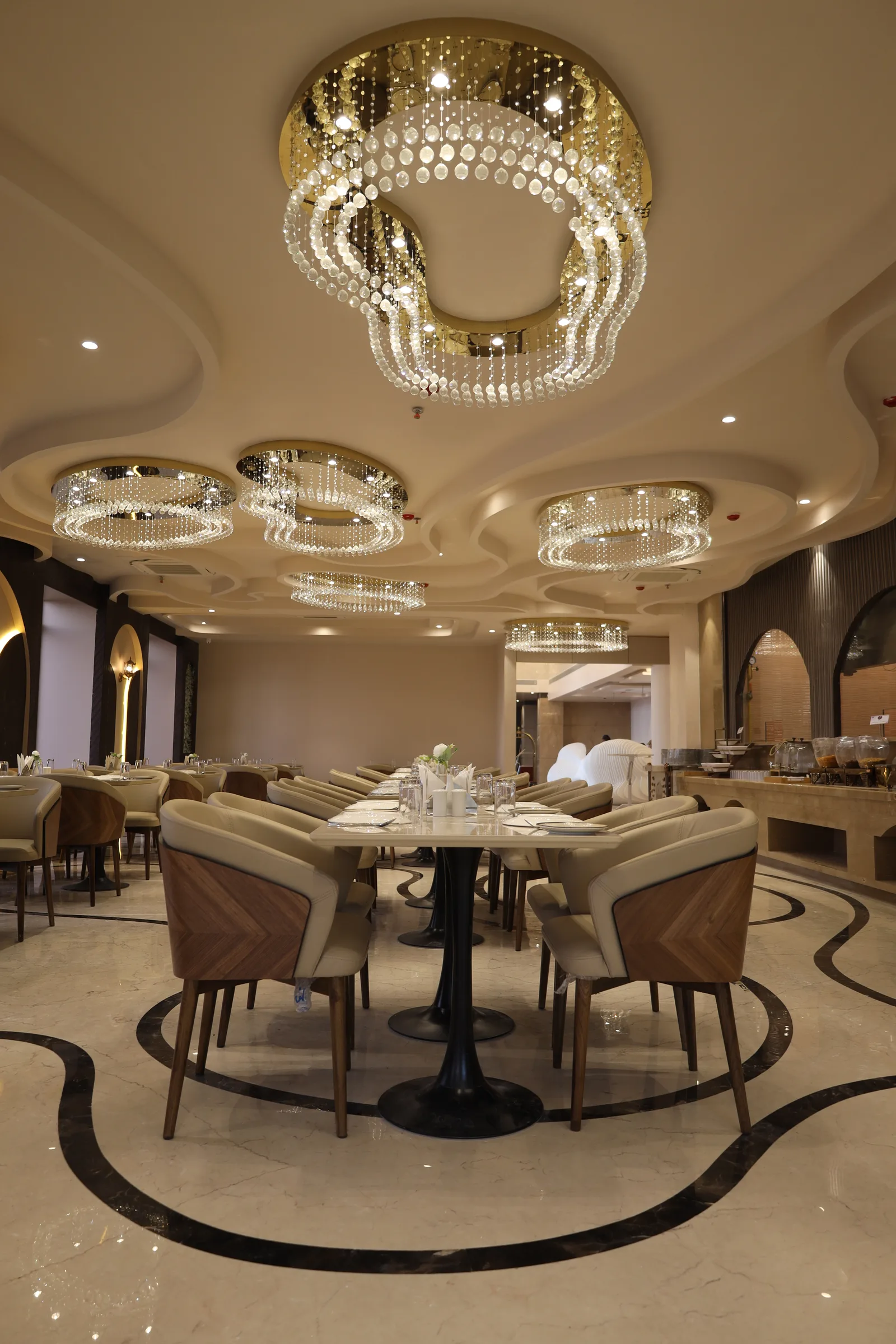 A long table laid in white linen at Kasturi, Vetiver Grand's pure vegetarian restaurant, crystal-and-gold chandelier medallions overhead.