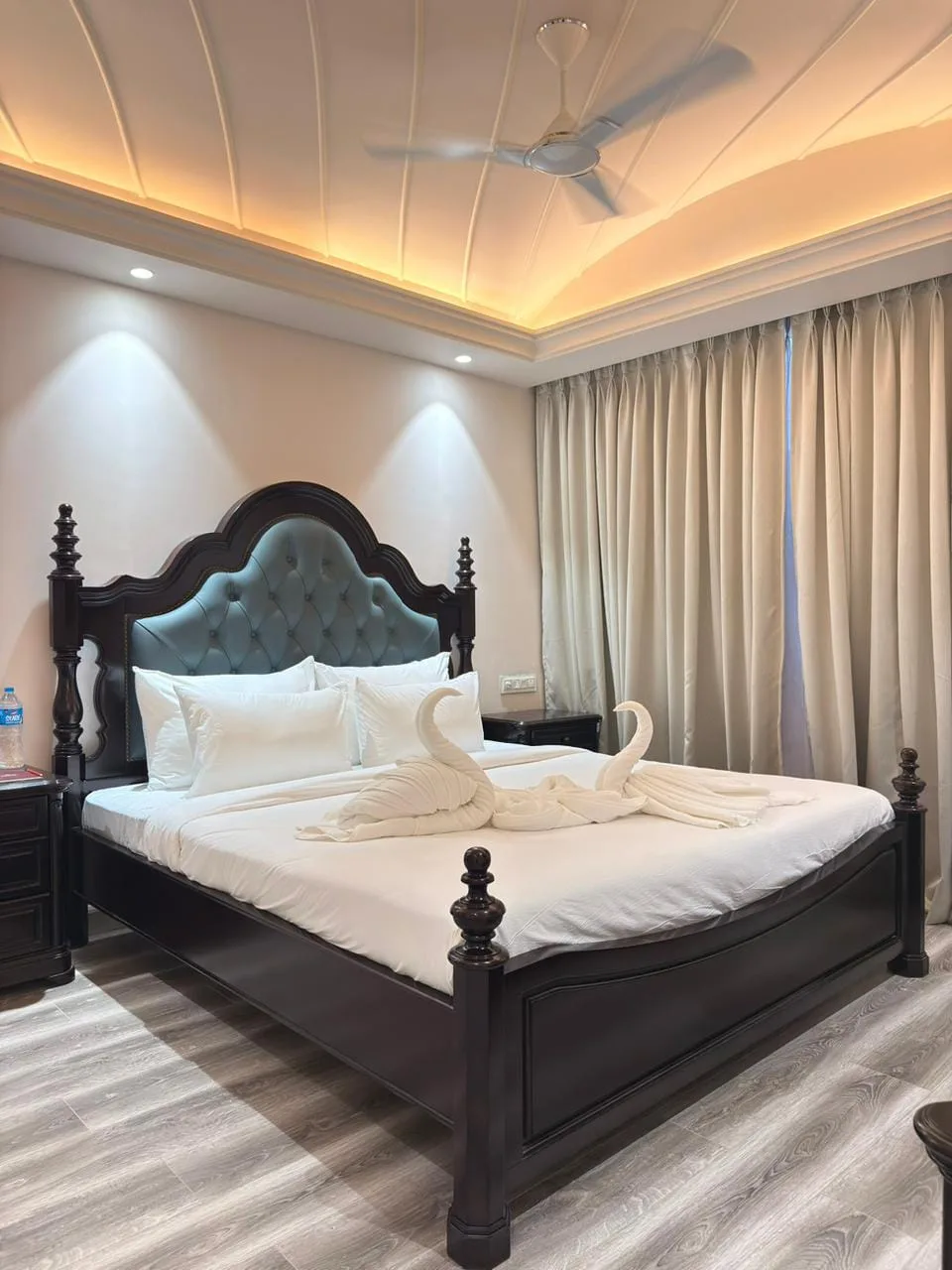Pool-facing suite at Vetiver Grand: carved four-poster king bed with a teal tufted headboard beneath an arched, gold-lit cove ceiling.